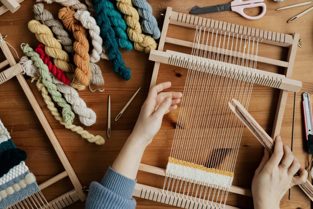 pexels photo 4219651 4219651 Top view of hands weaving on a wooden loom with colorful yarn, emphasizing craftsmanship and creativity.